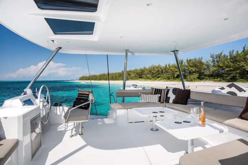 The shaded flybridge lounge with cushions, a table, glasses and a bottle of rosé, anchored off a beach