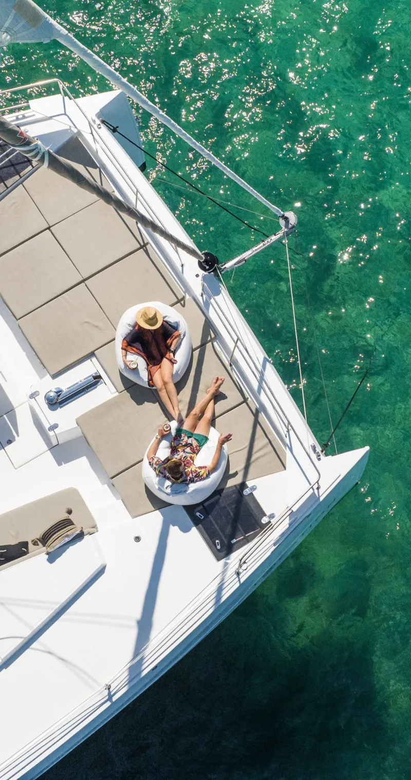 Two people relaxing on bean bags on the foredeck, seen from above, with clear green water below