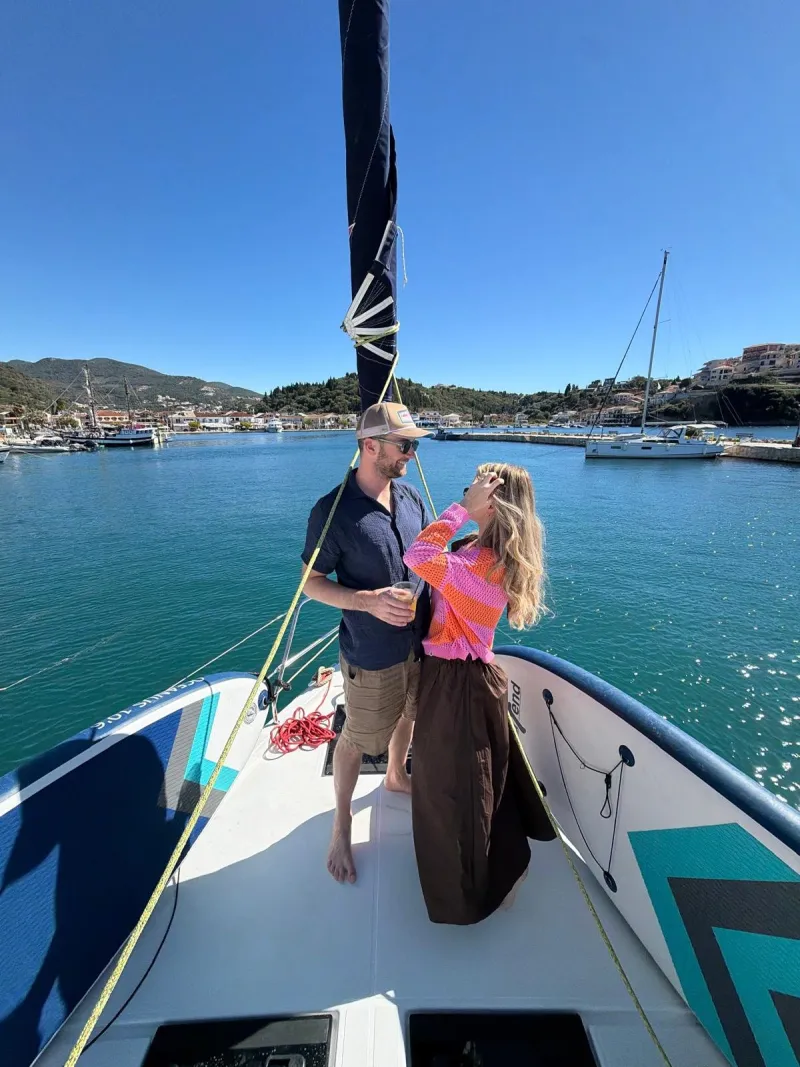 Lily and Nik on the bow of a sailboat in a turquoise harbour