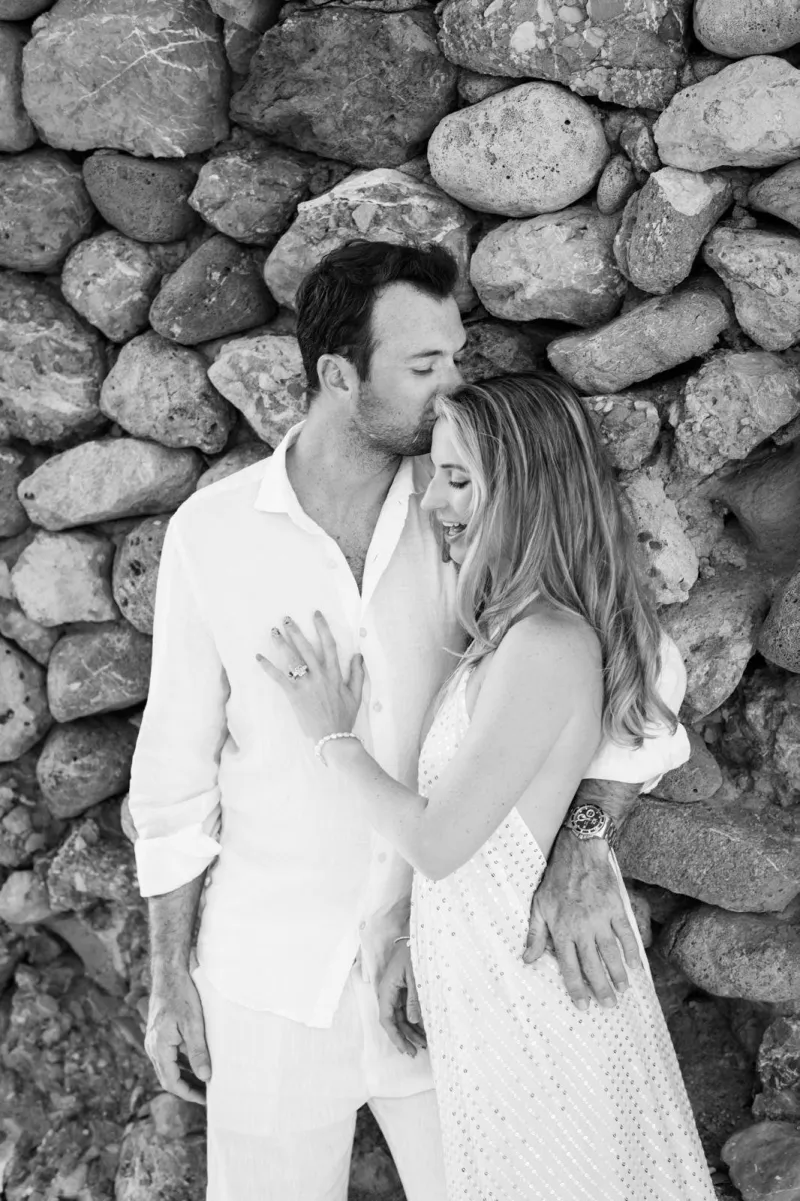 Black and white photo of Nik kissing Lily’s forehead in front of a stone wall