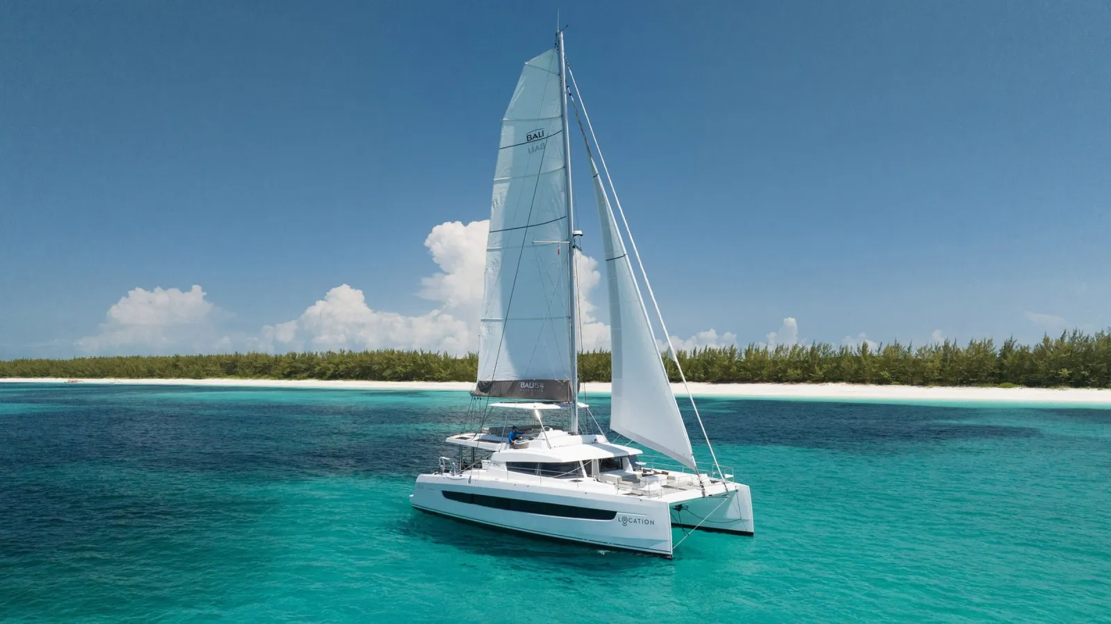 Location, a white catamaran under sail off a white sand beach in the Bahamas